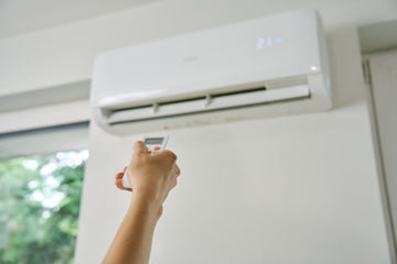 En person som justerar temperaturen på en luftvärmepump som sitter uppe på en vägg.