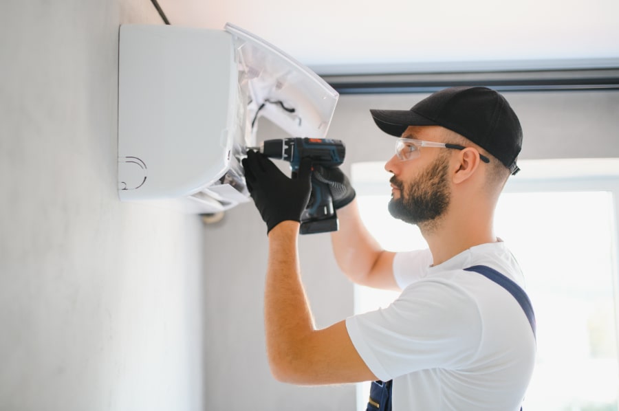 En person som installerar en luftvärmepump uppe på en vägg.slider_item_CwFQQc