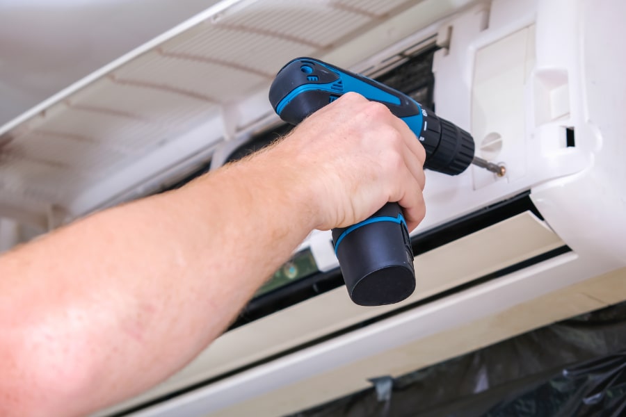 En person använder en batteridriven borrmaskin för att skruva i höljet på en väggmonterad inomhusenhet till en luftvärmepump.